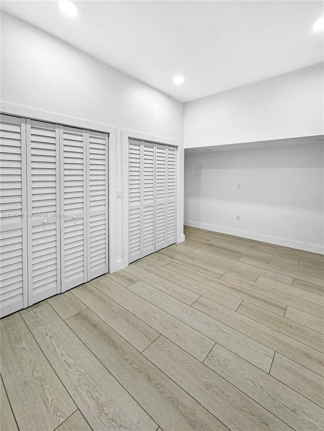 unfurnished bedroom with two closets, wood finished floors, and recessed lighting