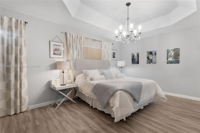 bedroom with a tray ceiling, wood finished floors, baseboards, and a notable chandelier