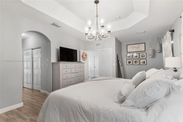 bedroom with visible vents, arched walkways, light wood-style floors, baseboards, and a chandelier