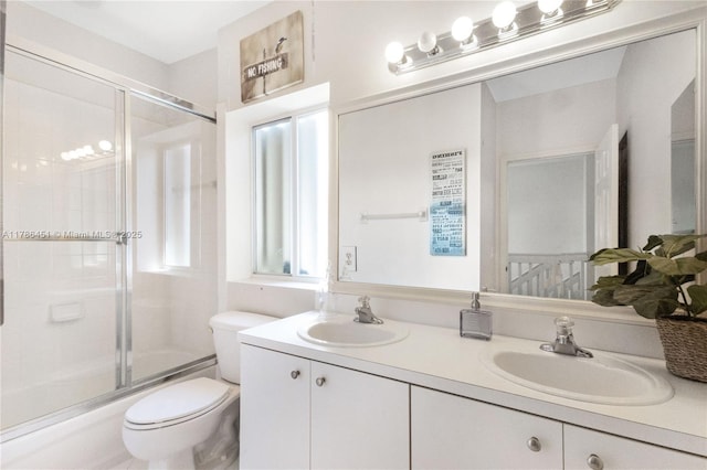 bathroom with combined bath / shower with glass door, a sink, double vanity, and toilet