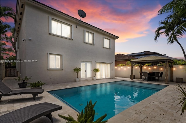 pool at dusk featuring a gazebo, a patio area, and an outdoor pool