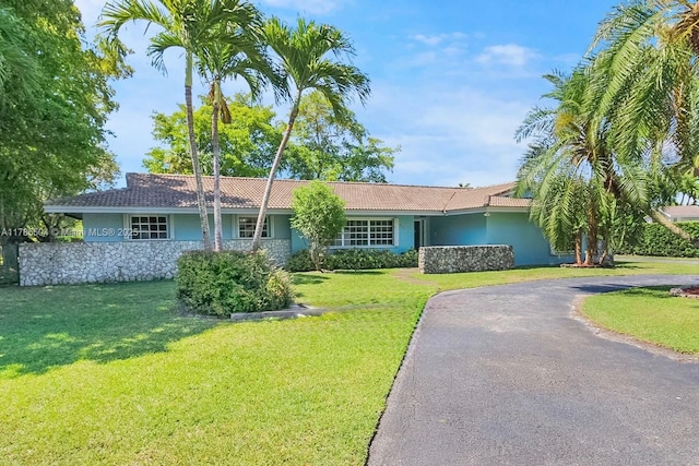 single story home featuring a tiled roof, a front yard, and stucco siding