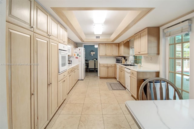 kitchen featuring a sink, white appliances, light brown cabinets, light countertops, and a raised ceiling