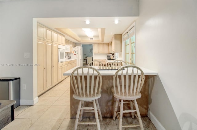 kitchen with a peninsula, a tray ceiling, baseboards, white appliances, and cream cabinetry