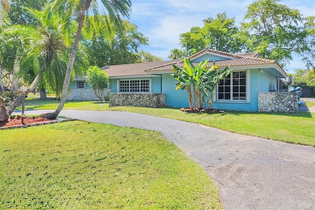 ranch-style home featuring stucco siding, a tile roof, a front lawn, and aphalt driveway