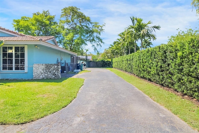 view of property exterior featuring aphalt driveway, a tiled roof, fence, a yard, and stucco siding