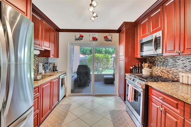 kitchen with light tile patterned floors, decorative backsplash, a sink, appliances with stainless steel finishes, and light stone countertops