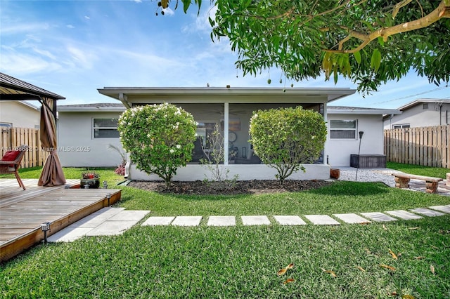 rear view of property with stucco siding, a yard, fence, a wooden deck, and a sunroom