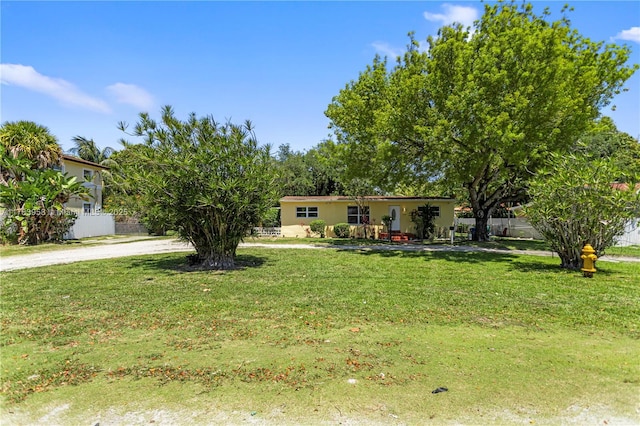 manufactured / mobile home with stucco siding, dirt driveway, a front yard, and fence