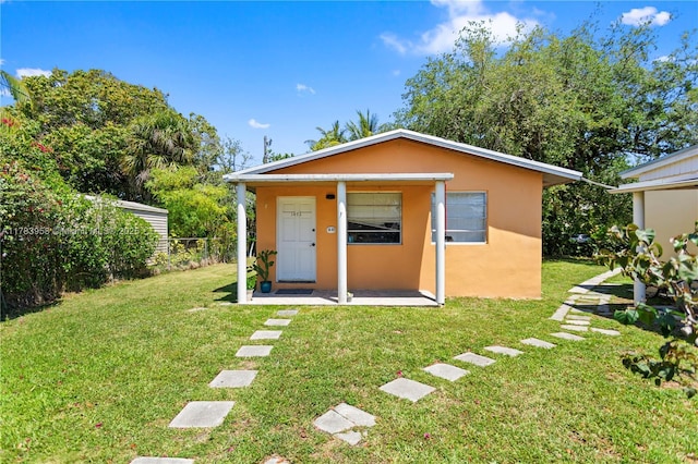 back of property featuring stucco siding, fence, and a lawn