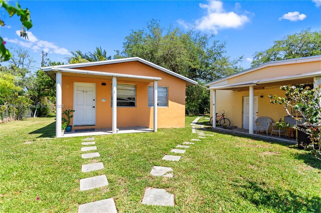 rear view of property featuring a lawn, stucco siding, and fence