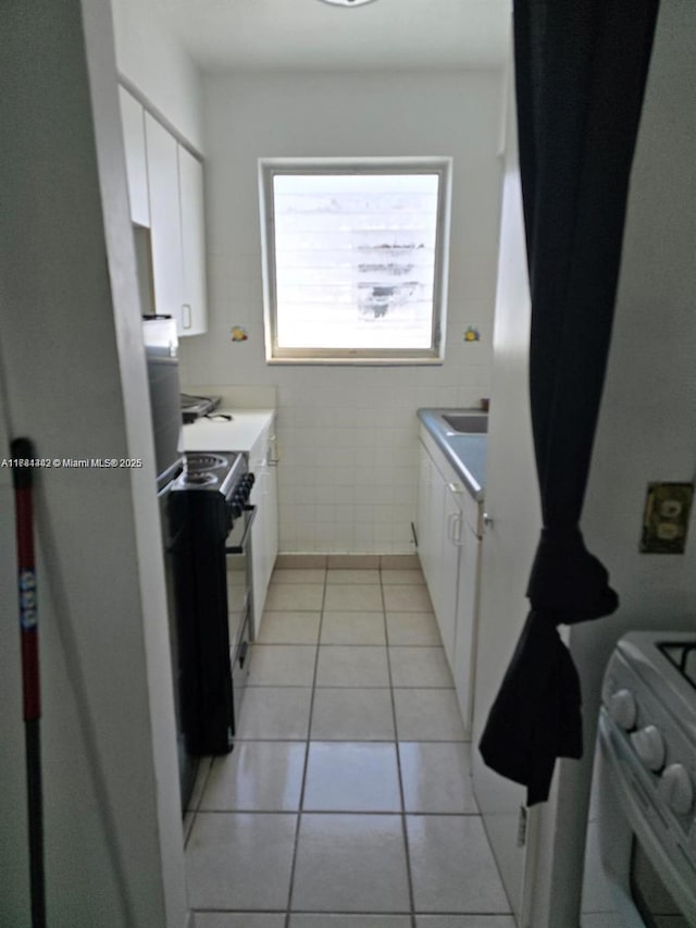 200 76th St Unit 57, Miami Beach, FL 33141 - kitchen with white range with gas stovetop, white cabinetry, tile walls, black / electric stove, and light tile patterned floors