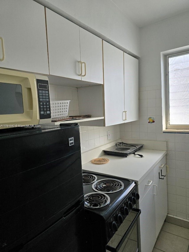 200 76th St Unit 57, Miami Beach, FL 33141 - kitchen with black appliances, light countertops, white cabinetry, tile walls, and light tile patterned flooring