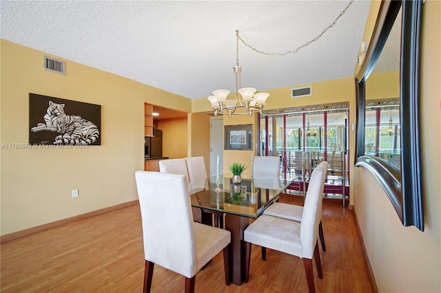 dining space featuring a textured ceiling, baseboards, visible vents, a notable chandelier, and wood finished floors