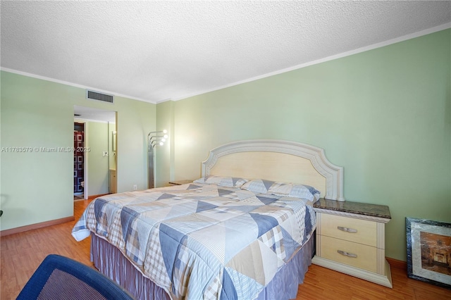bedroom featuring wood finished floors, visible vents, a textured ceiling, and crown molding