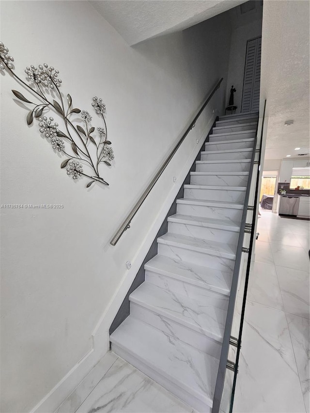 stairs with marble finish floor and a textured ceiling