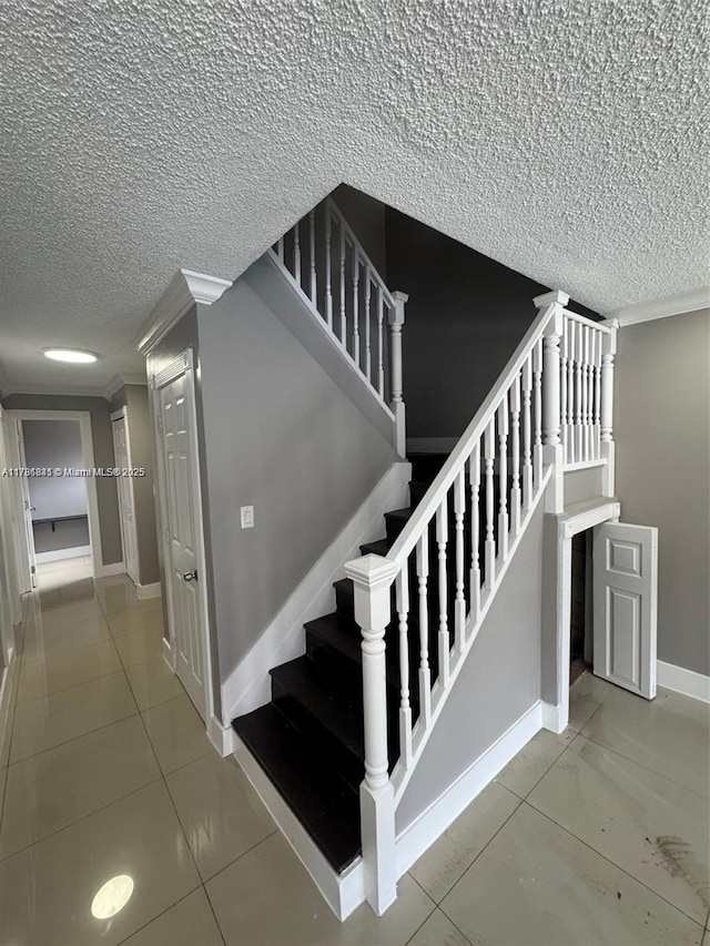 stairway featuring tile patterned flooring, baseboards, a textured ceiling, and ornamental molding
