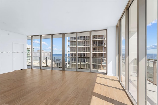 spare room with expansive windows, wood finished floors, a water view, and plenty of natural light