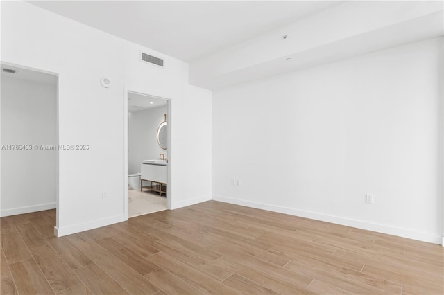unfurnished bedroom featuring a walk in closet, baseboards, visible vents, and light wood finished floors