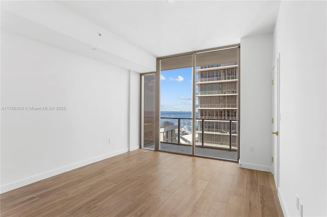 unfurnished room with baseboards, wood finished floors, floor to ceiling windows, and a water view