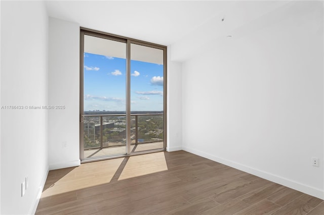 unfurnished room featuring baseboards, a wall of windows, and wood finished floors