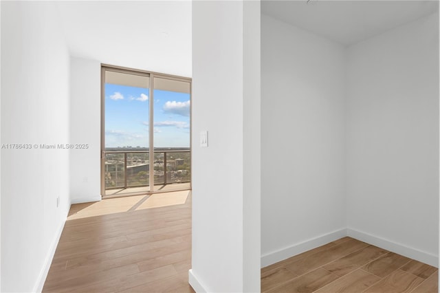 empty room featuring expansive windows, wood finished floors, and baseboards