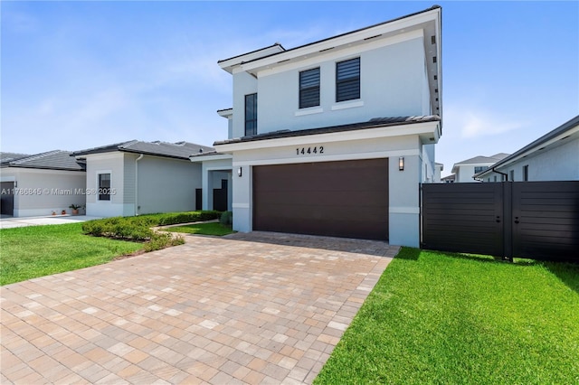 view of front facade with a front lawn, stucco siding, decorative driveway, an attached garage, and fence