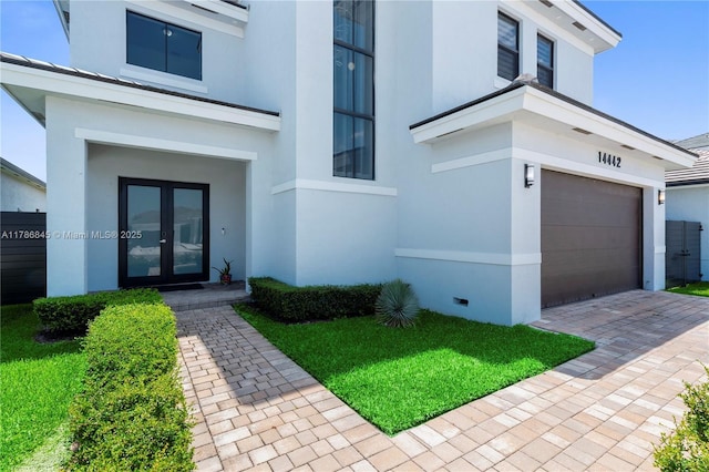 view of front of home featuring stucco siding, decorative driveway, french doors, and a garage