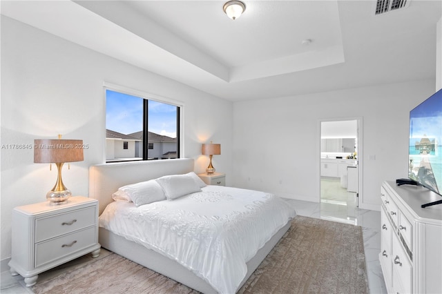 bedroom with connected bathroom, visible vents, a raised ceiling, and baseboards