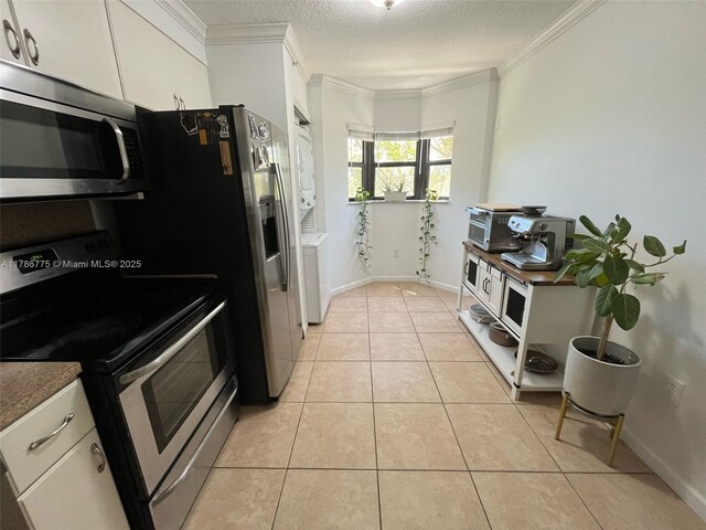 22701 SW 88th Pl Unit 203-9, Cutler Bay, FL 33190 - kitchen with stainless steel appliances, stacked washer and clothes dryer, white cabinets, light tile patterned flooring, and ornamental molding