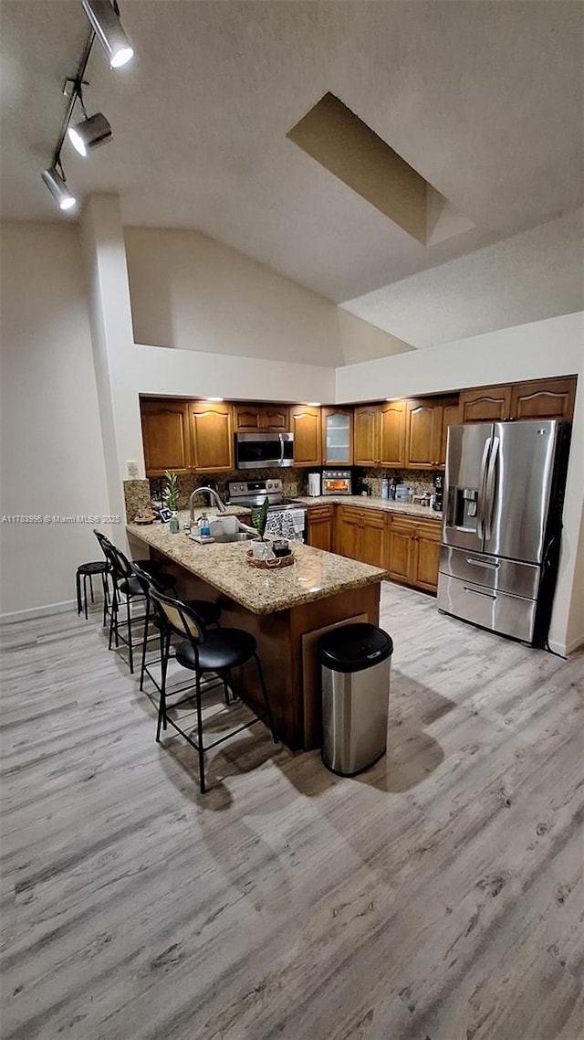 kitchen with stainless steel appliances, a peninsula, a sink, and light wood-style flooring