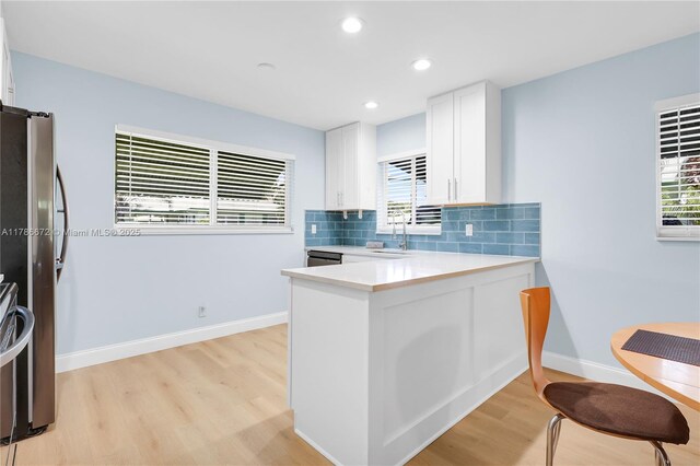 632 Hummingbird Ln, Delray Beach, FL 33445 - kitchen with stainless steel dishwasher, a sink, light wood-style floors, a peninsula, and white cabinets