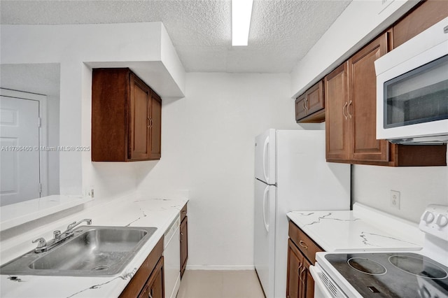 kitchen featuring a sink, a textured ceiling, baseboards, white appliances, and light stone countertops