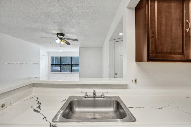 kitchen featuring light countertops, a sink, dark brown cabinetry, a textured ceiling, and ceiling fan