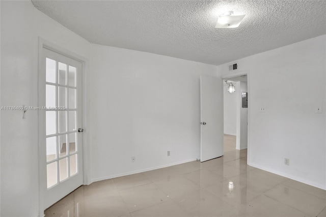 unfurnished room with baseboards, tile patterned flooring, a textured ceiling, and visible vents