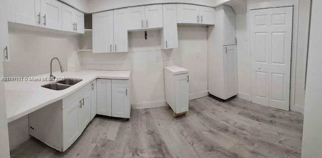 kitchen featuring light wood finished floors, white cabinets, a sink, baseboards, and light countertops