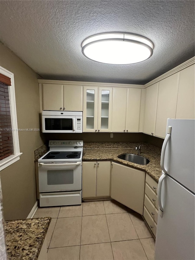 kitchen with cream cabinetry, a sink, white appliances, and a textured ceiling