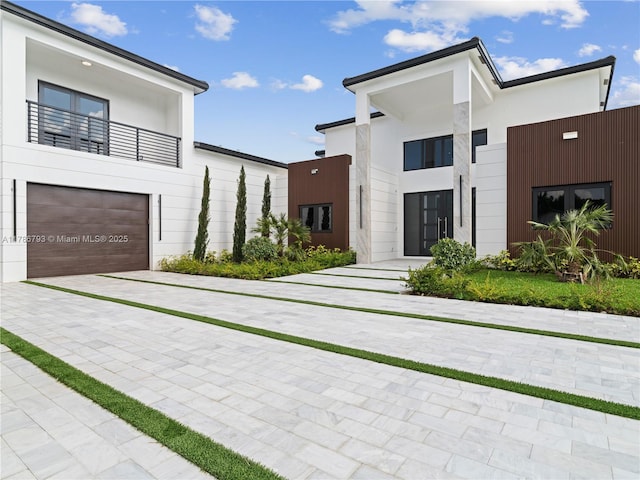 modern home with stucco siding, driveway, a balcony, and a garage