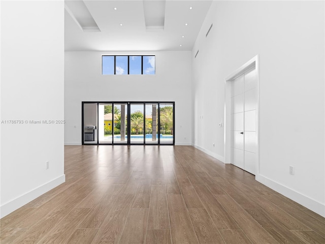 unfurnished living room featuring baseboards, wood finished floors, and a high ceiling