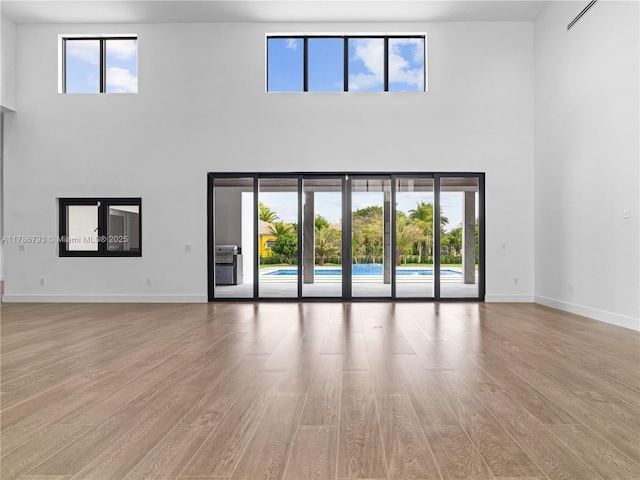 unfurnished living room with light wood finished floors, a towering ceiling, and baseboards