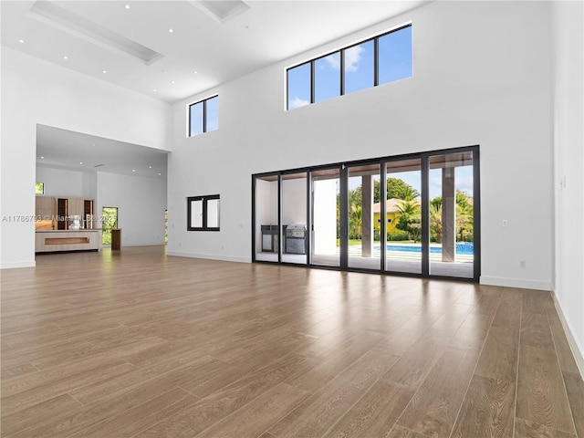 unfurnished living room featuring a towering ceiling, wood finished floors, and baseboards