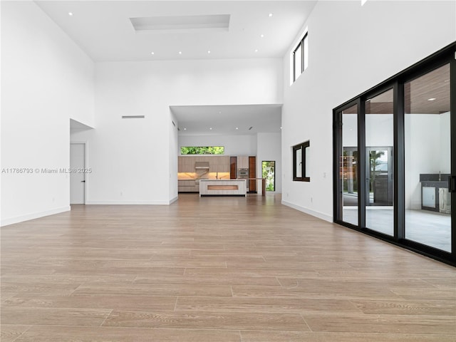 unfurnished living room featuring baseboards, light wood-style flooring, a towering ceiling, and a healthy amount of sunlight