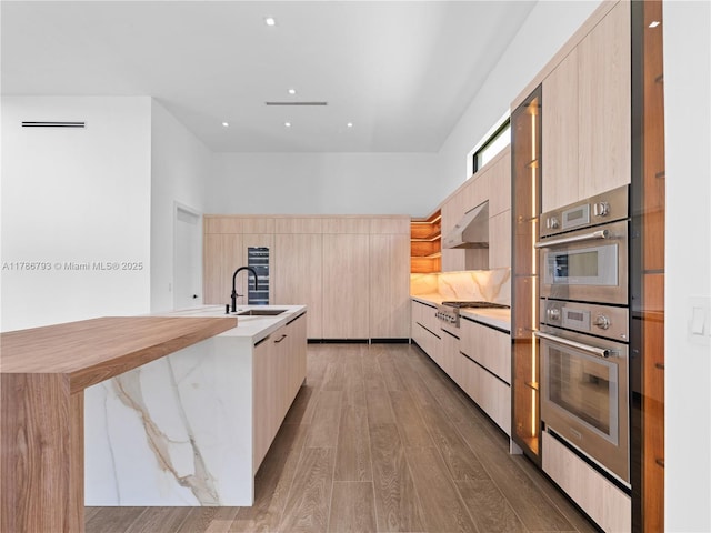 kitchen with light wood finished floors, modern cabinets, light brown cabinets, and a sink