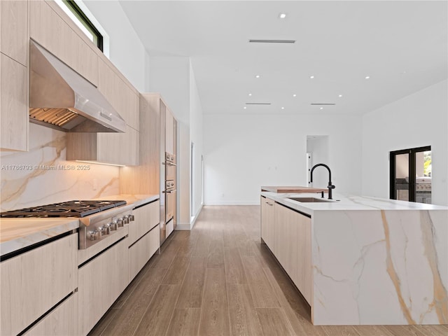 kitchen with stainless steel gas cooktop, light brown cabinetry, a sink, ventilation hood, and modern cabinets