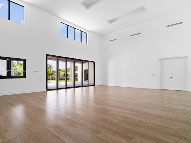 unfurnished room featuring baseboards, wood finished floors, a towering ceiling, and recessed lighting