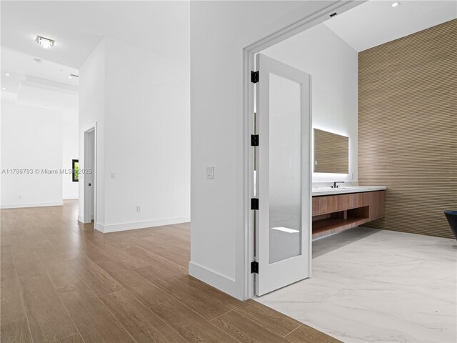 corridor with a high ceiling, baseboards, recessed lighting, and light wood-style floors