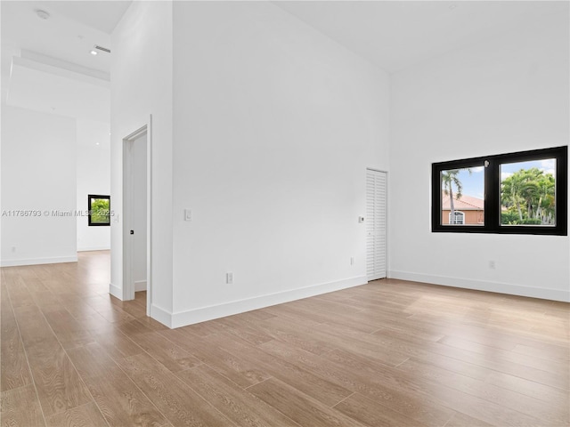 empty room with light wood-type flooring, a healthy amount of sunlight, and a towering ceiling