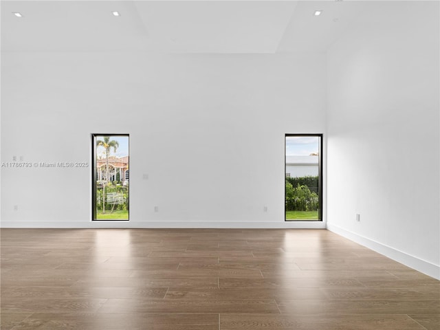 spare room with recessed lighting, wood finished floors, a towering ceiling, and baseboards