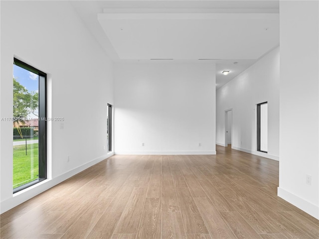 unfurnished room with light wood finished floors, a towering ceiling, and baseboards