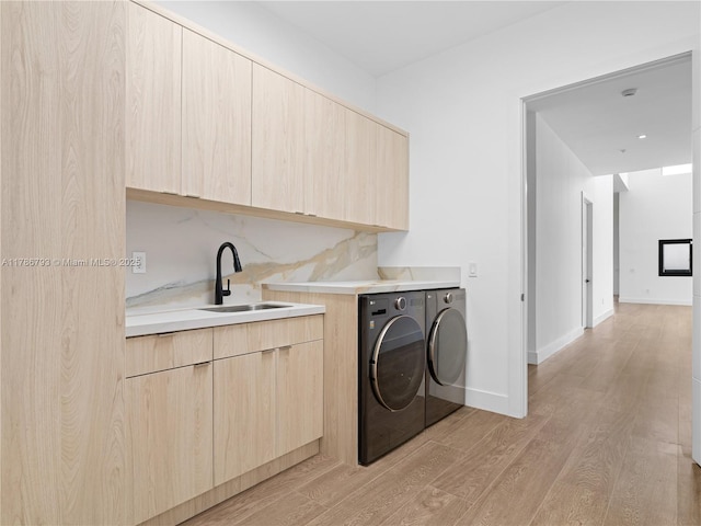 washroom with a sink, light wood-type flooring, baseboards, separate washer and dryer, and cabinet space